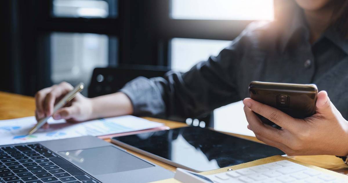 Vrouw met een pen en een telefoon in haar hand berekent financiële zaken achter een latop 